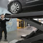 Mechanic carefully examining car on hydraulic lift in automotive workshop, ensuring safety and performance.